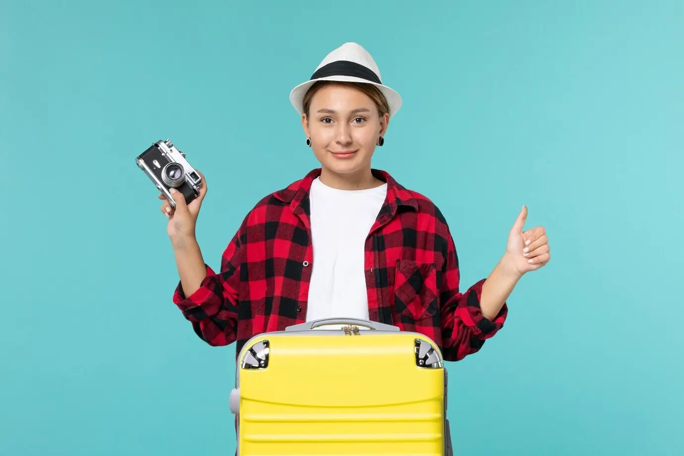 Vorderansicht einer jungen Frau, die auf eine Reise geht und eine Kamera hält, vor einem hellblauen Hintergrund.